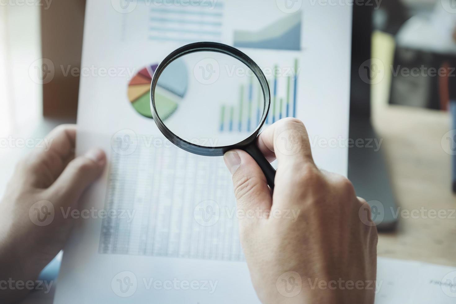 Business man using magnifying to review balance sheet annual with using laptop computer to calculating budget photo