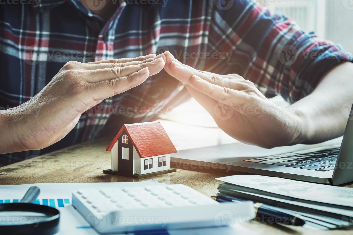 Insurance agent raises his hand hand protecting a house under his hands photo