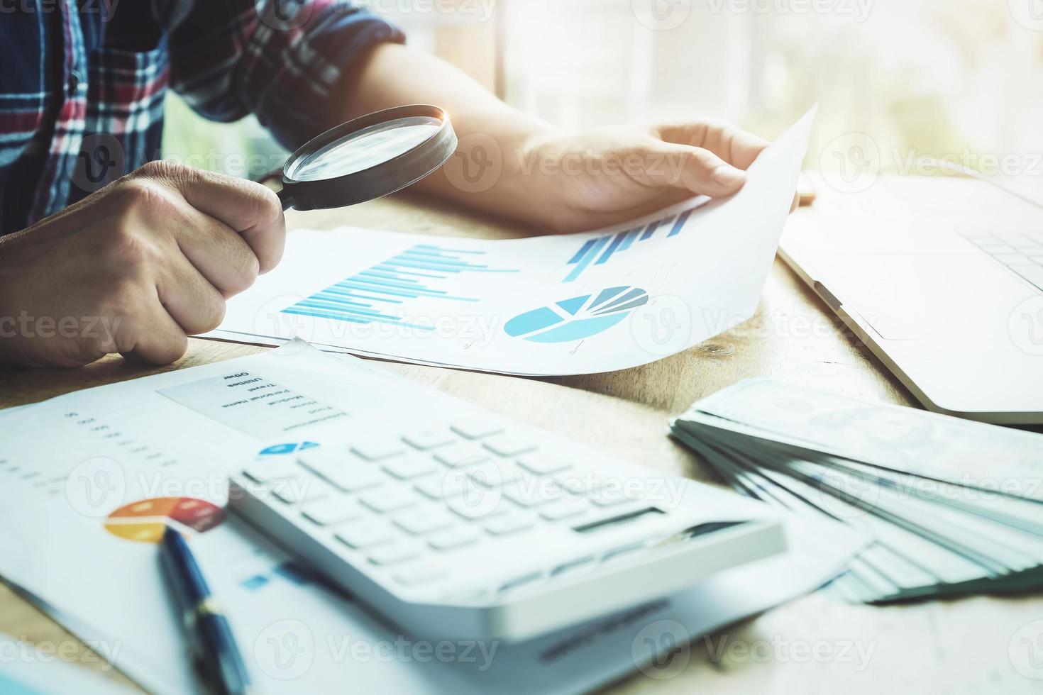 Business man using magnifying to review balance sheet annual with using calculator and laptop computer to calculating budget photo