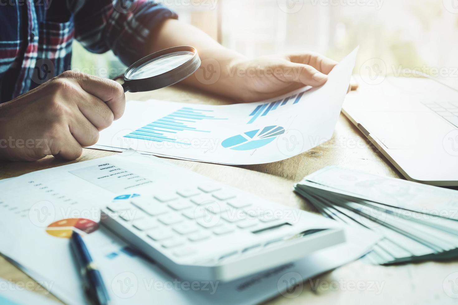 Hombre de negocios con lupa para revisar el balance anual con calculadora y computadora portátil para calcular el presupuesto foto