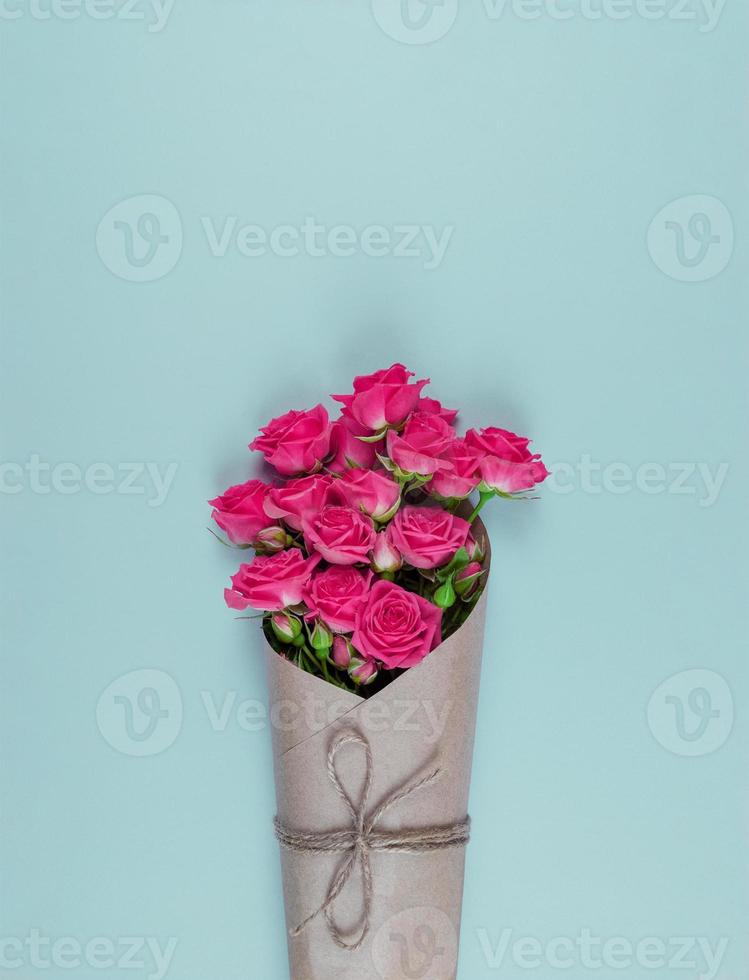 Bouquet of small flowered pink roses wrapped in craft paper on blue background photo