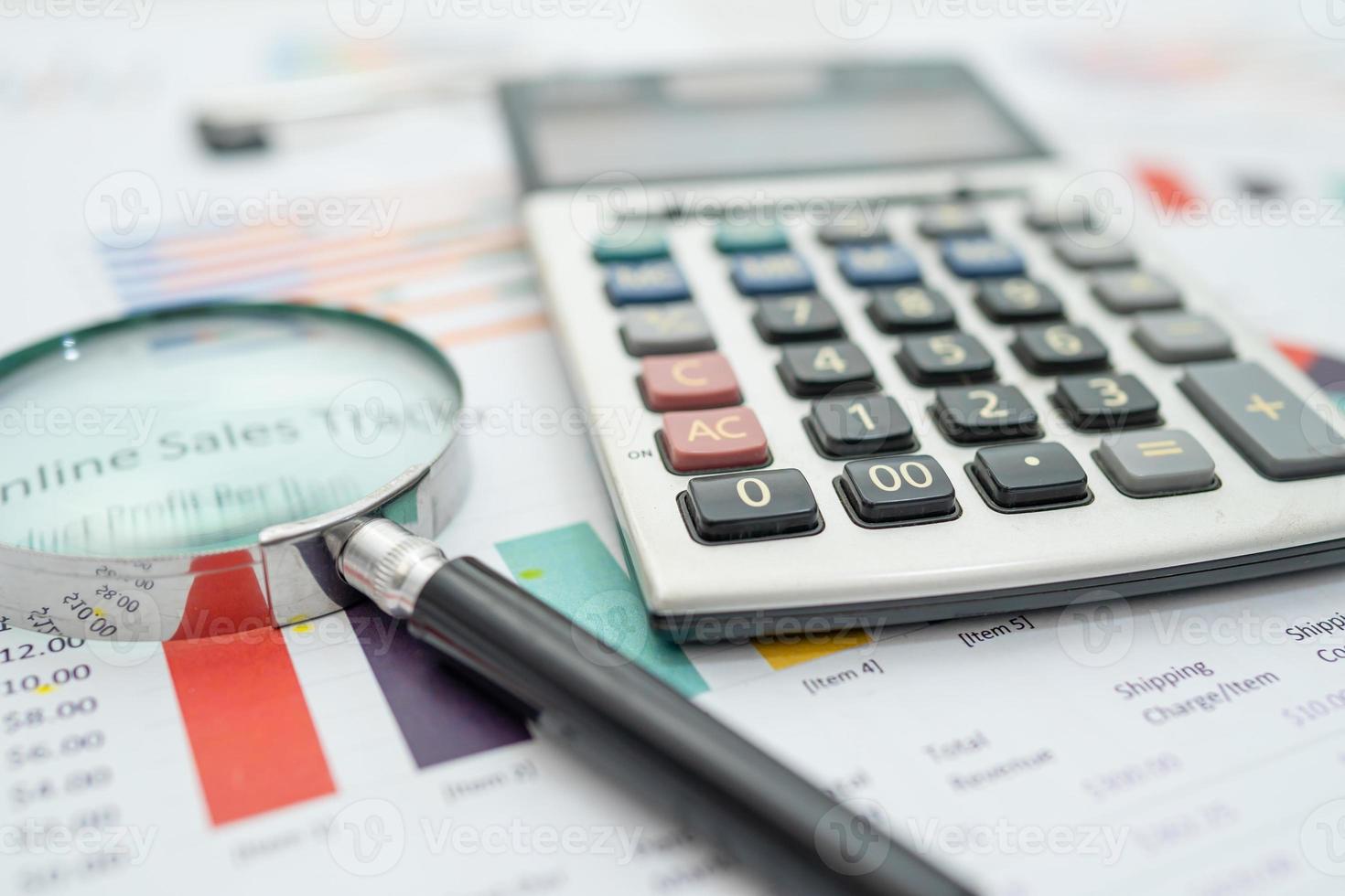 Magnifying glass  and calculator on charts graphs paper photo