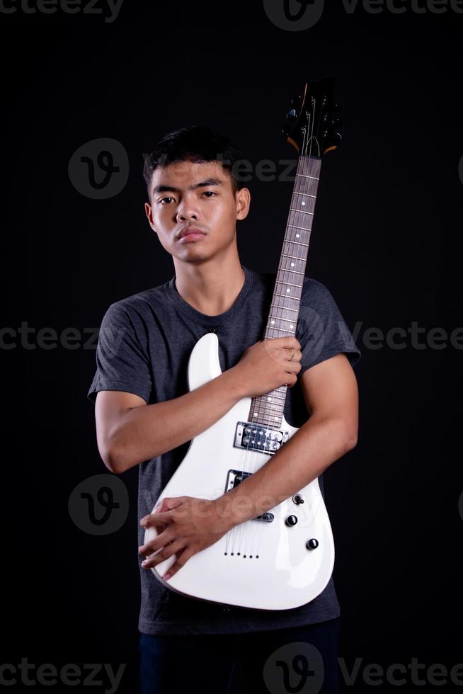 Young man in black leather jacket with electric guitar against black background in studio photo