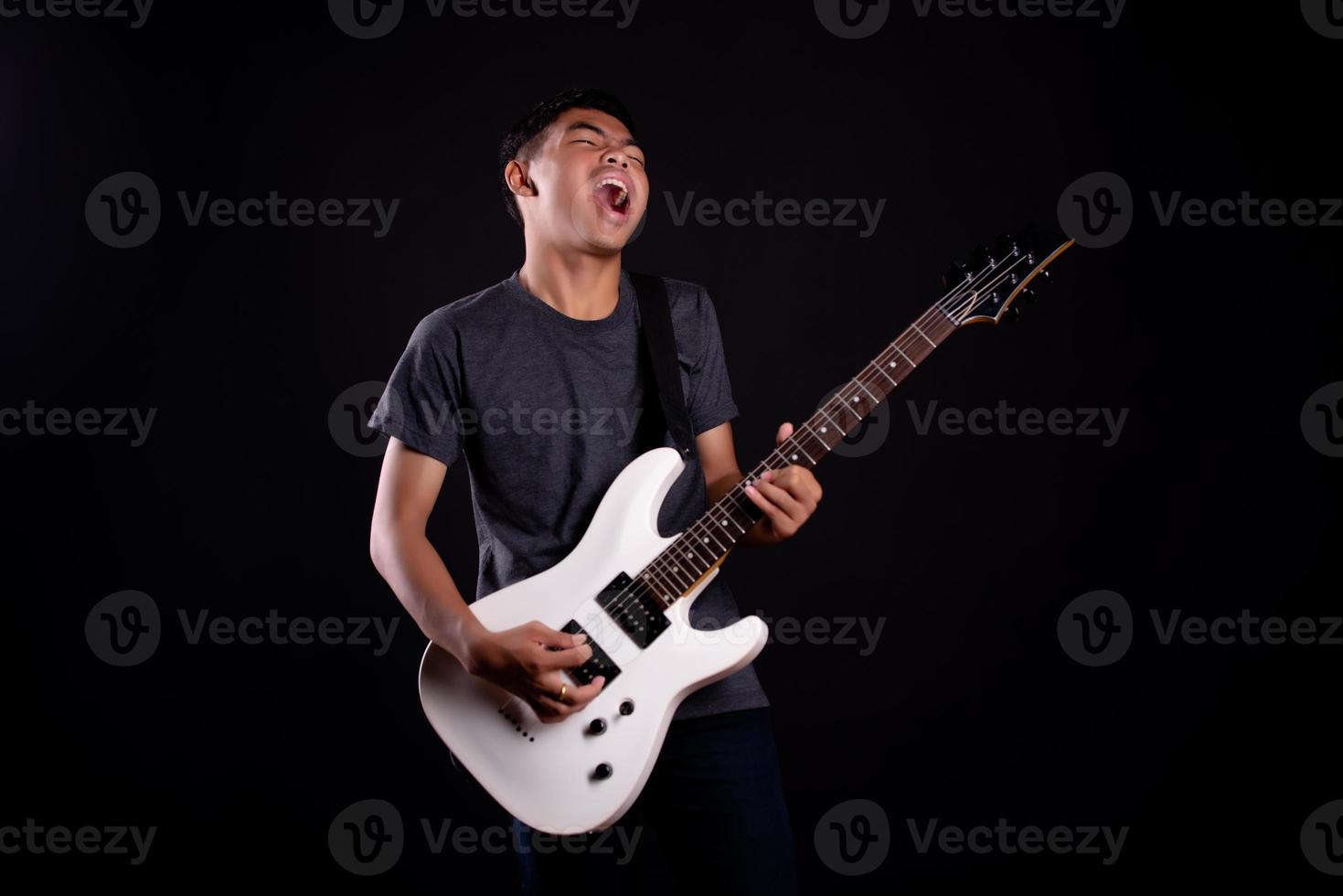 Joven en chaqueta de cuero negro con guitarra eléctrica contra fondo negro en studio foto