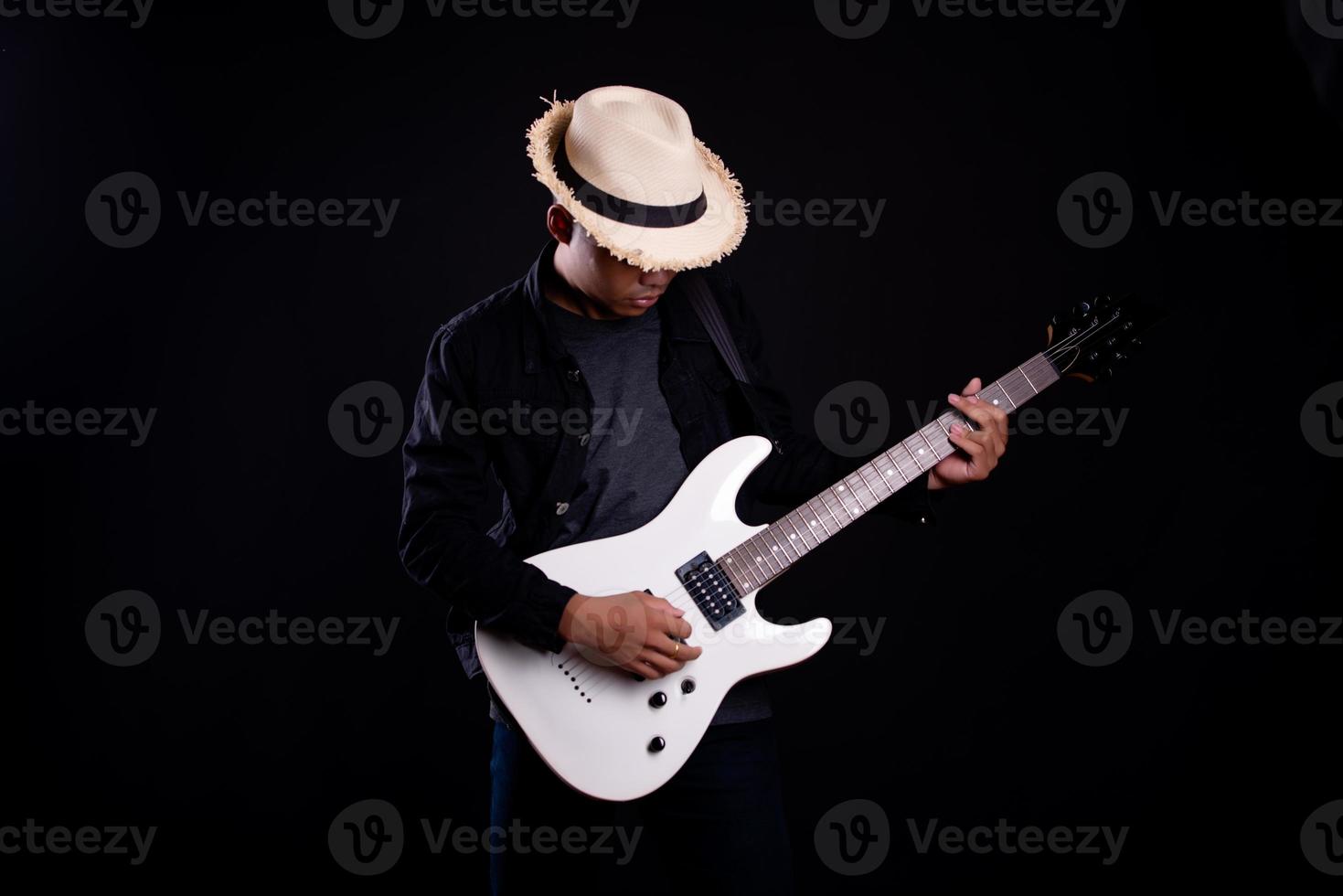 Joven en chaqueta de cuero negro con guitarra eléctrica contra fondo negro en studio foto