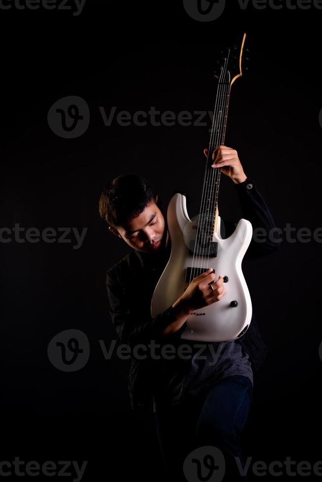 Young man in black leather jacket with electric guitar against black background in studio photo