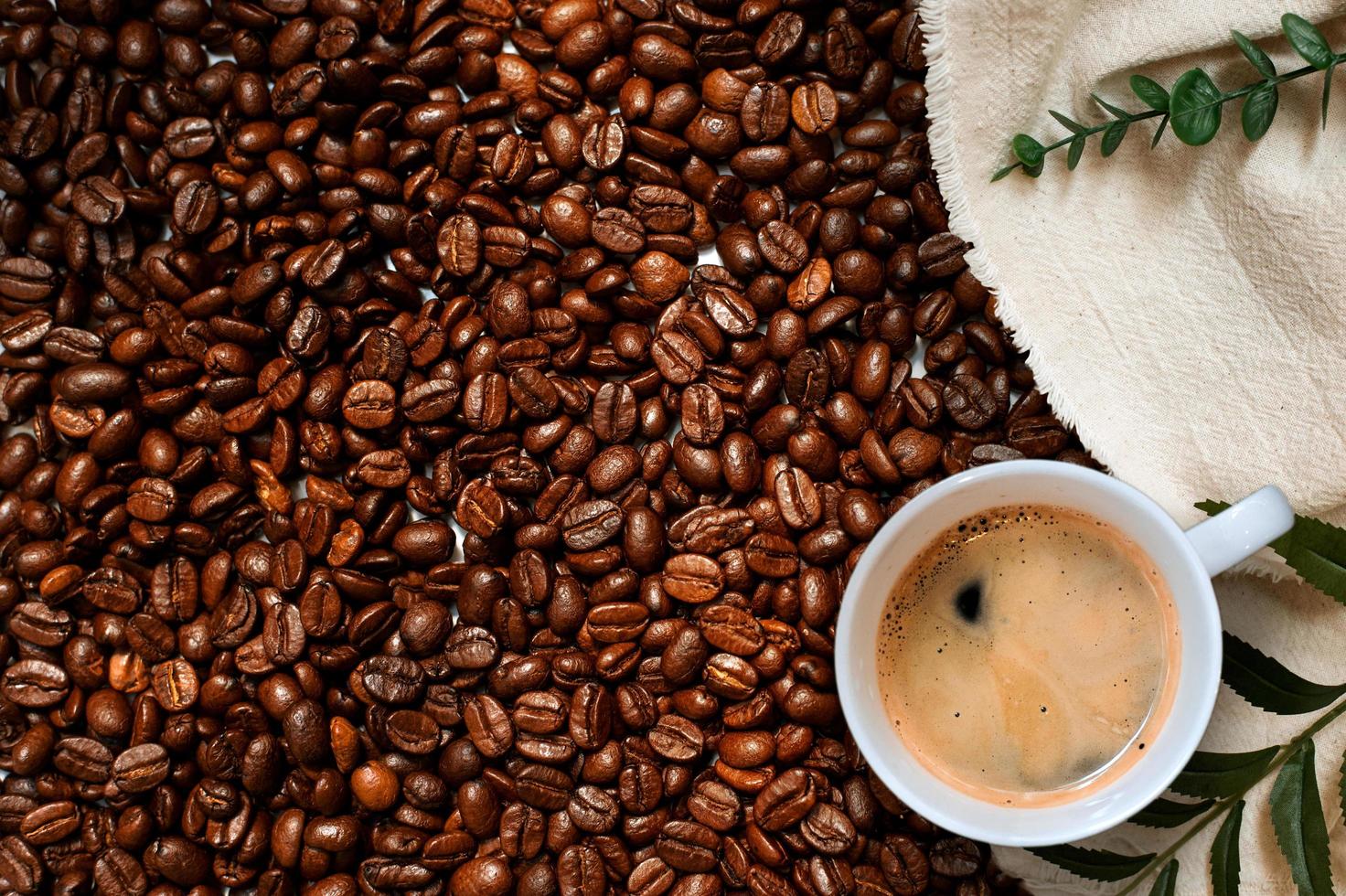 Top view of cup of coffee next to a cloth in pile of coffee beans photo