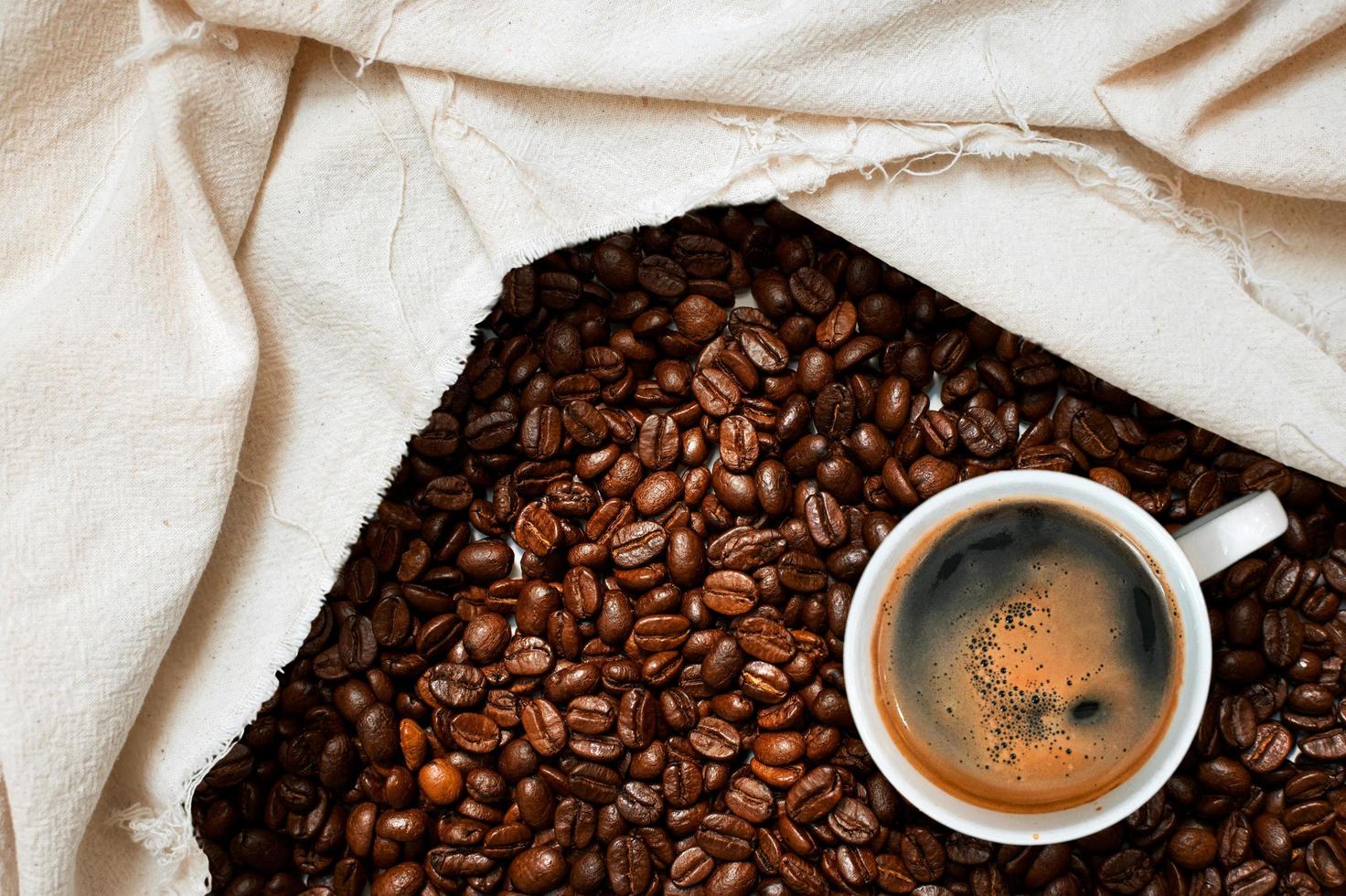 Top view of cup of coffee next to a cloth in pile of coffee beans photo