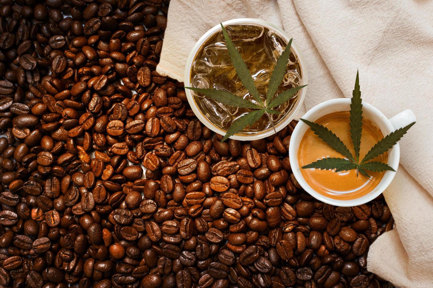 Cannabis leaves in two cups of coffee on a white tablecloth in a pile of coffee beans photo