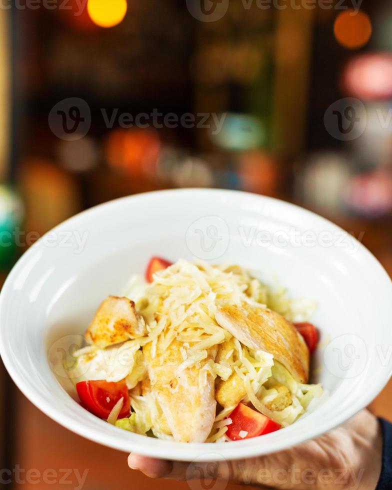 Man holding Caesar salad in the white plate with tomatoes from top photo