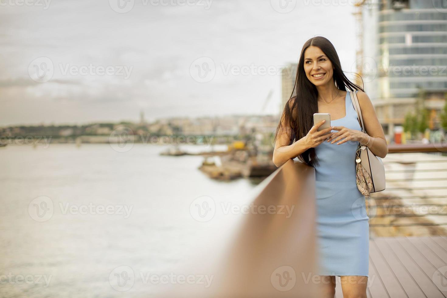 Mujer joven con un teléfono móvil mientras está de pie en el paseo fluvial foto