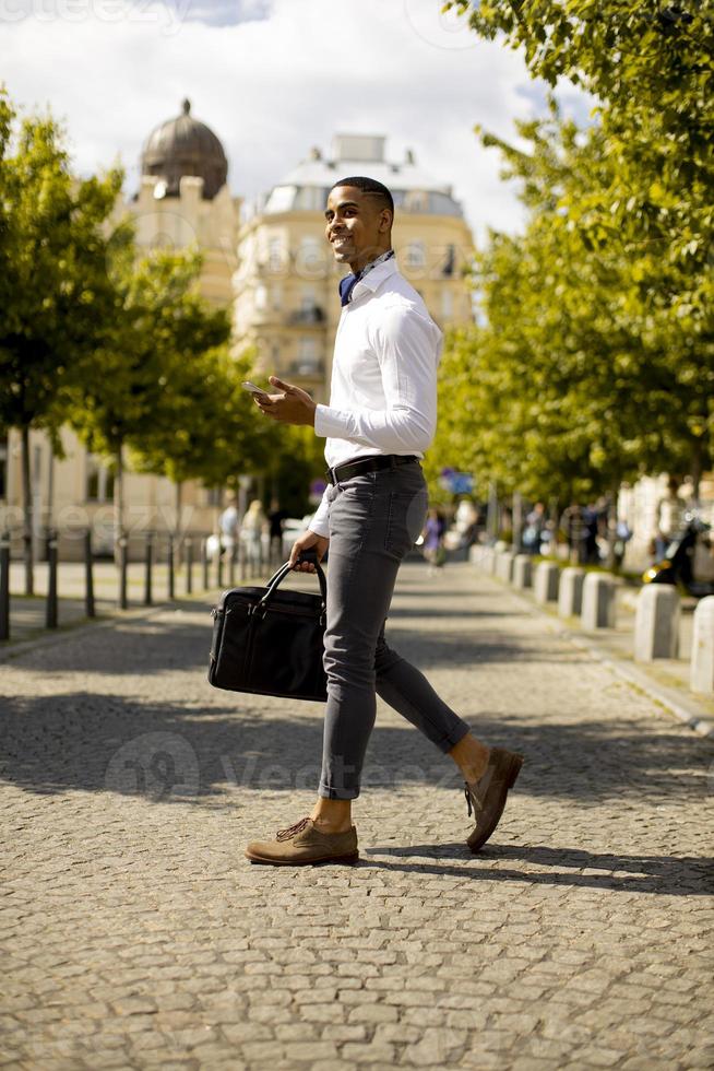 Joven empresario afroamericano usando un teléfono móvil mientras cruza una calle foto