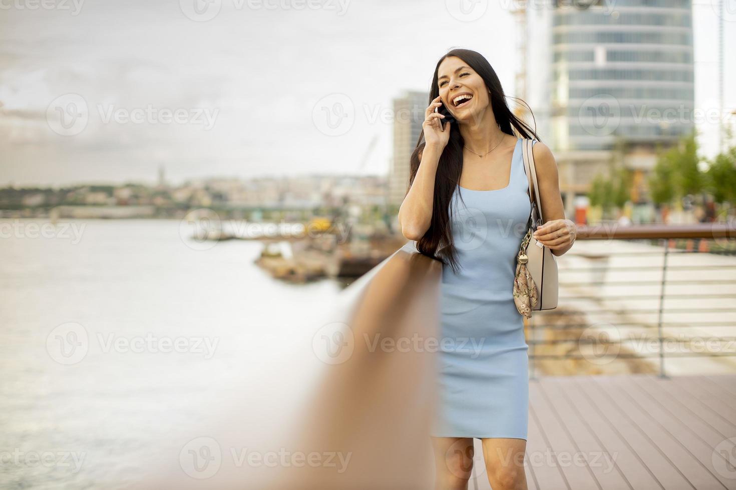 Mujer joven con un teléfono móvil mientras está de pie en el paseo fluvial foto