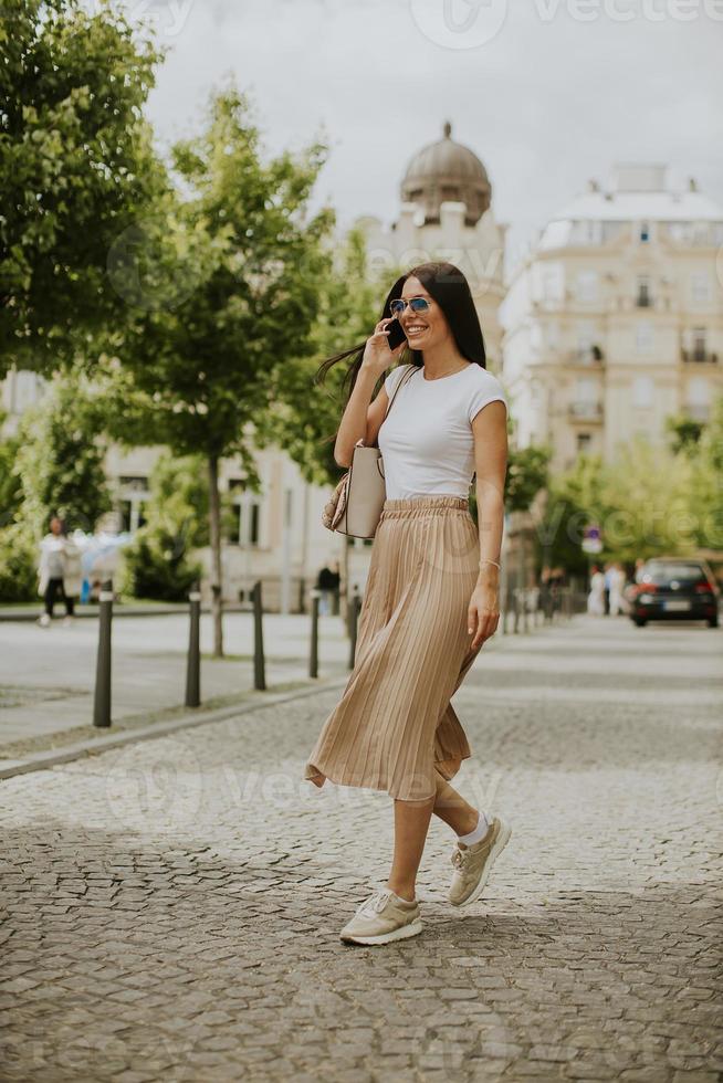 Mujer joven con un teléfono móvil mientras camina por la calle foto