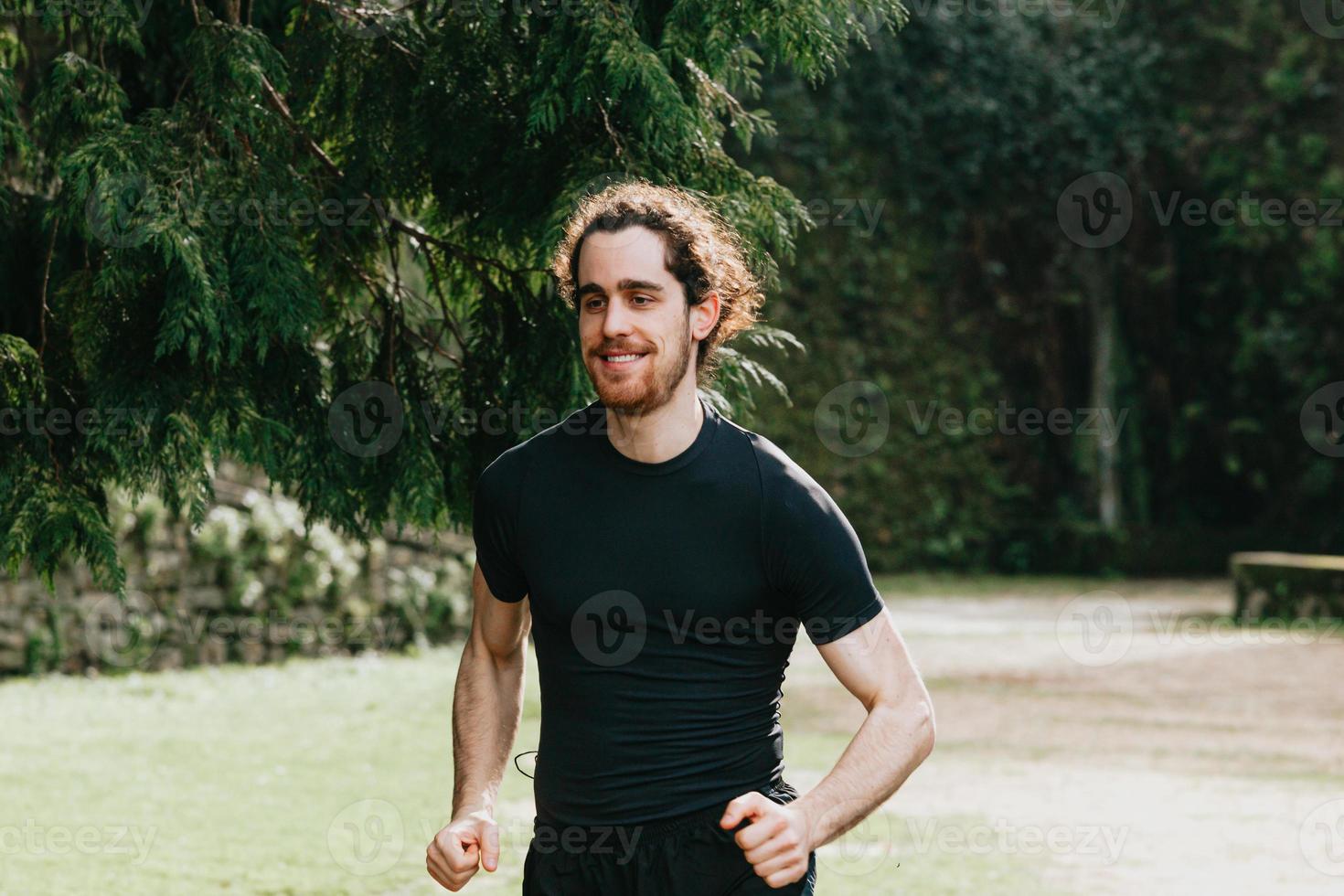 Un primer plano de un hombre de pelo largo corriendo entre los árboles durante un día soleado en el parque foto