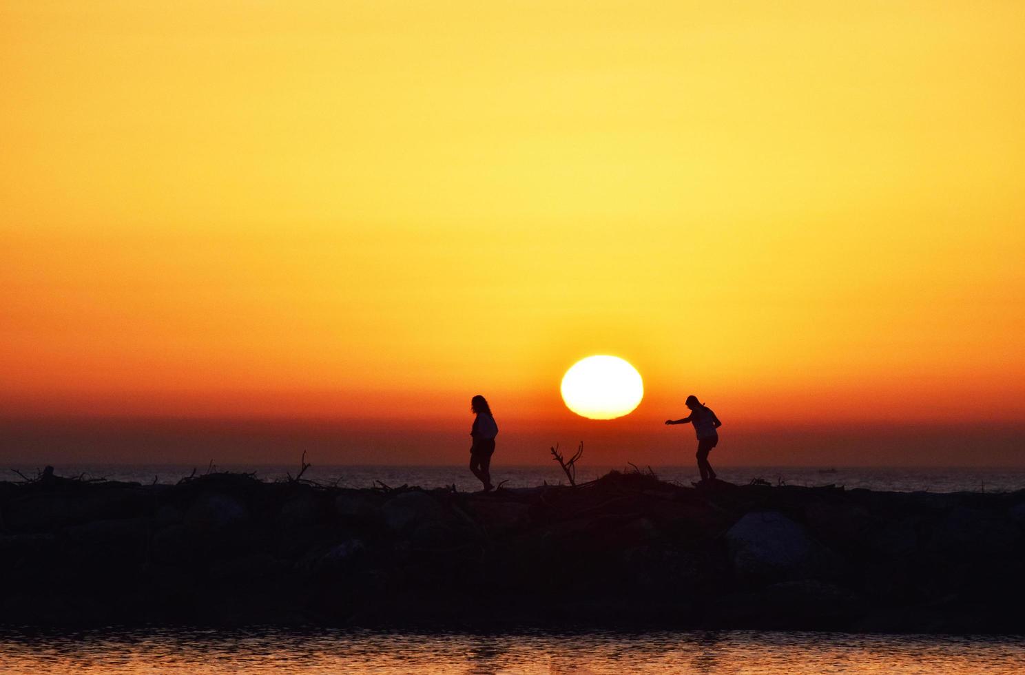 silueta de personas de pie sobre una roca durante la puesta de sol foto