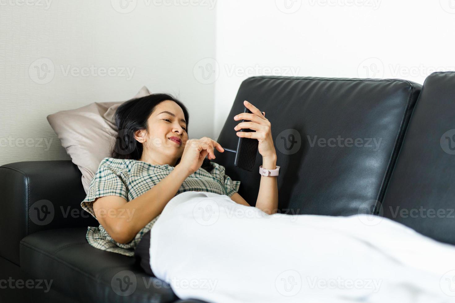 Mujer con teléfono inteligente mientras está acostado en el sofá concepto de cuarentena foto