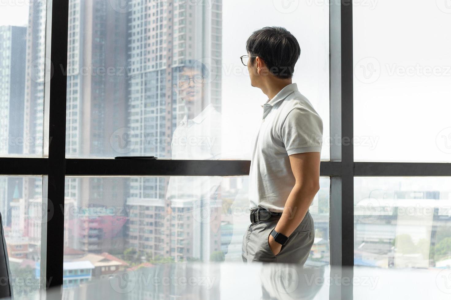 Businessman standing in office building looking through window photo