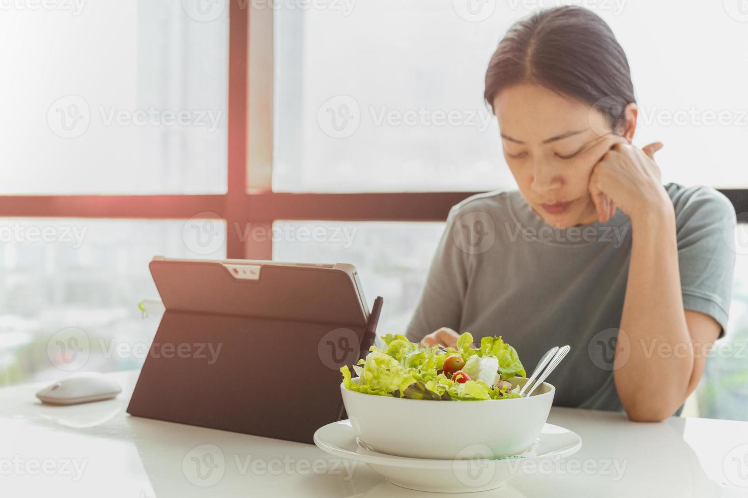 Selected focus on bowl of vegetable salad with woman working on laptop photo