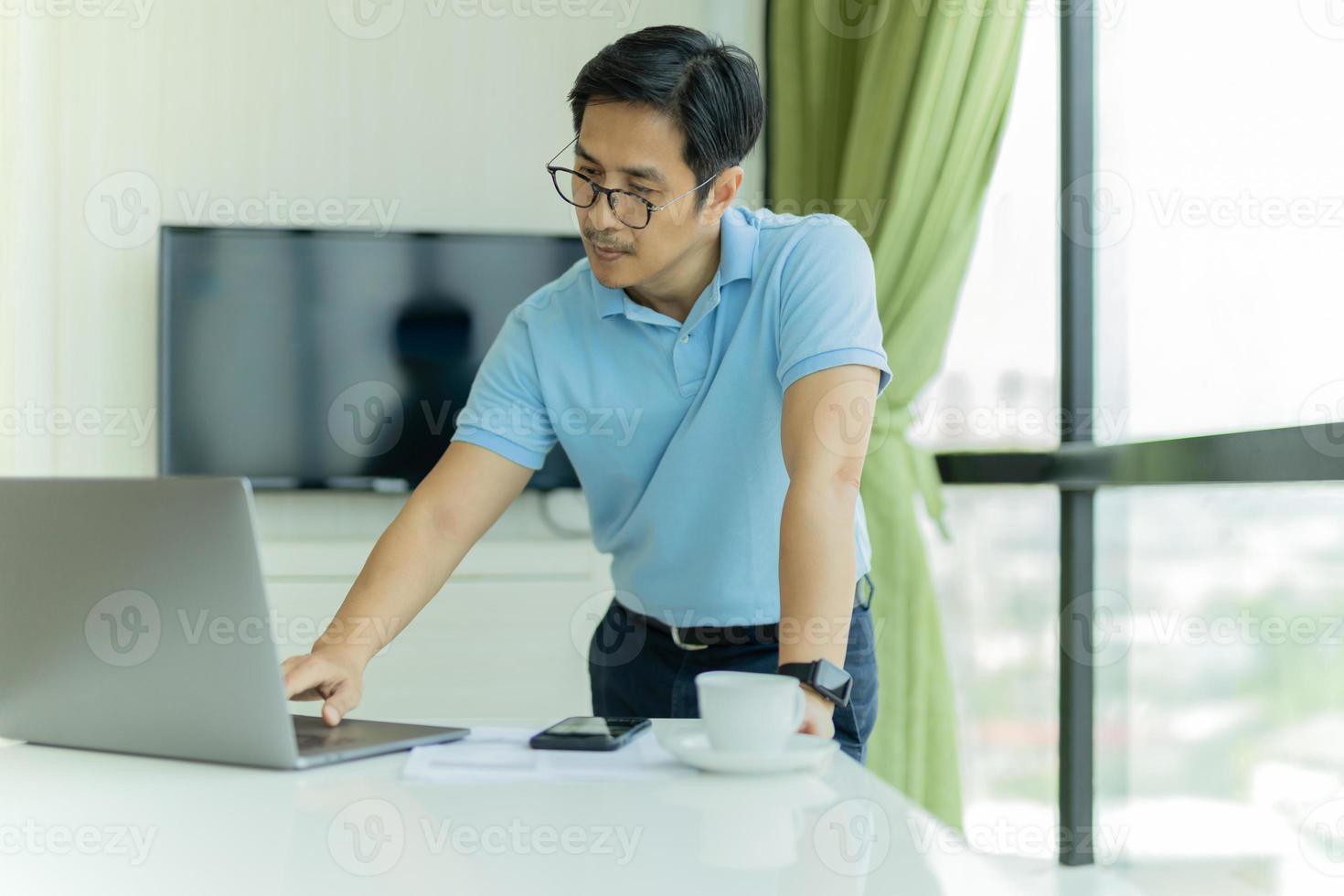 Businessman in glasses leaning over table and work on laptop in office photo