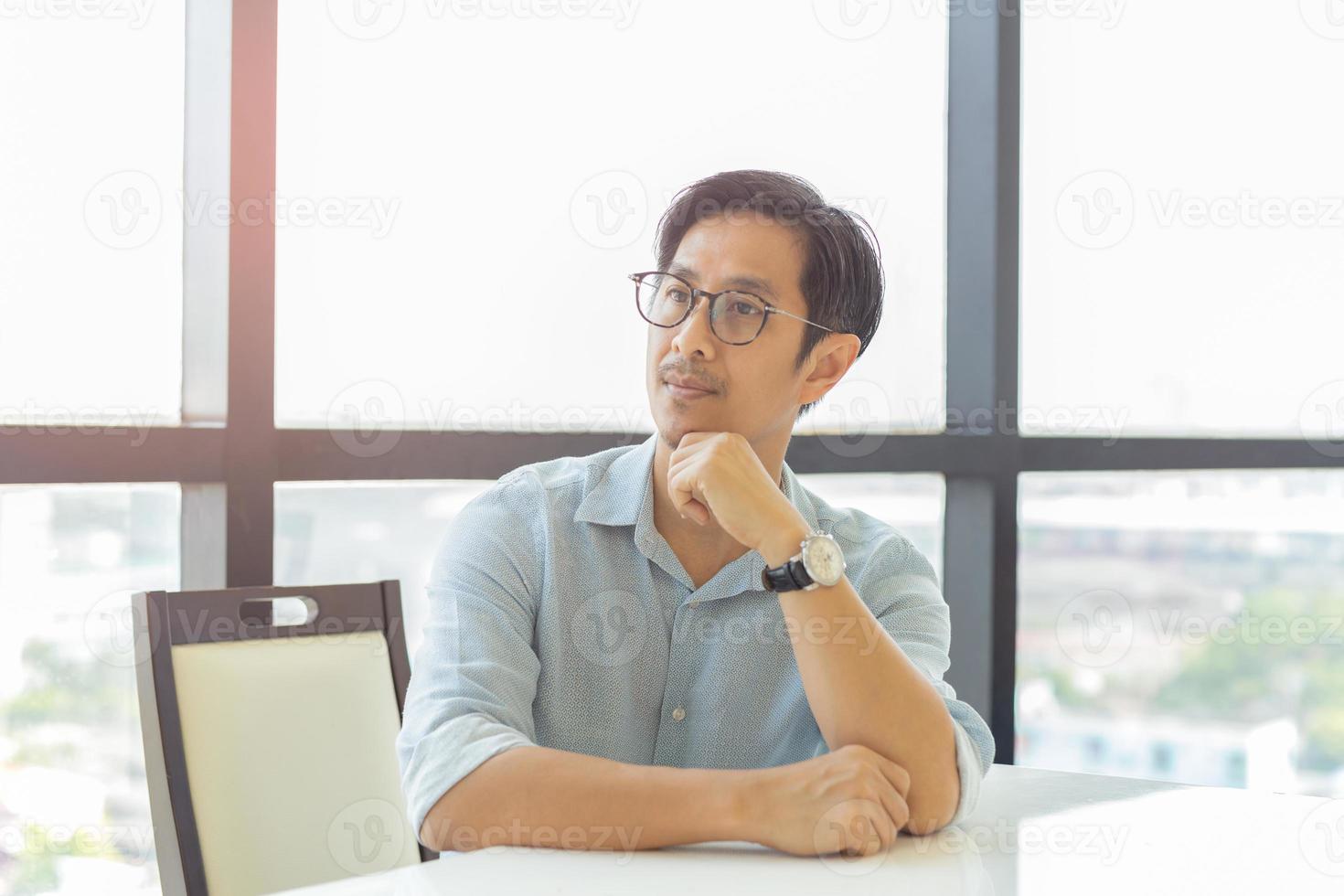 Portrait of businessman in eyeglasses sit at table resting with hand on his chin photo