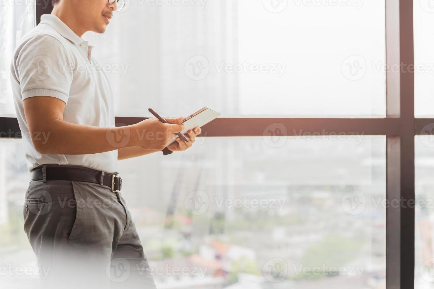 empresario de pie junto a la ventana en su oficina sosteniendo tableta digital foto