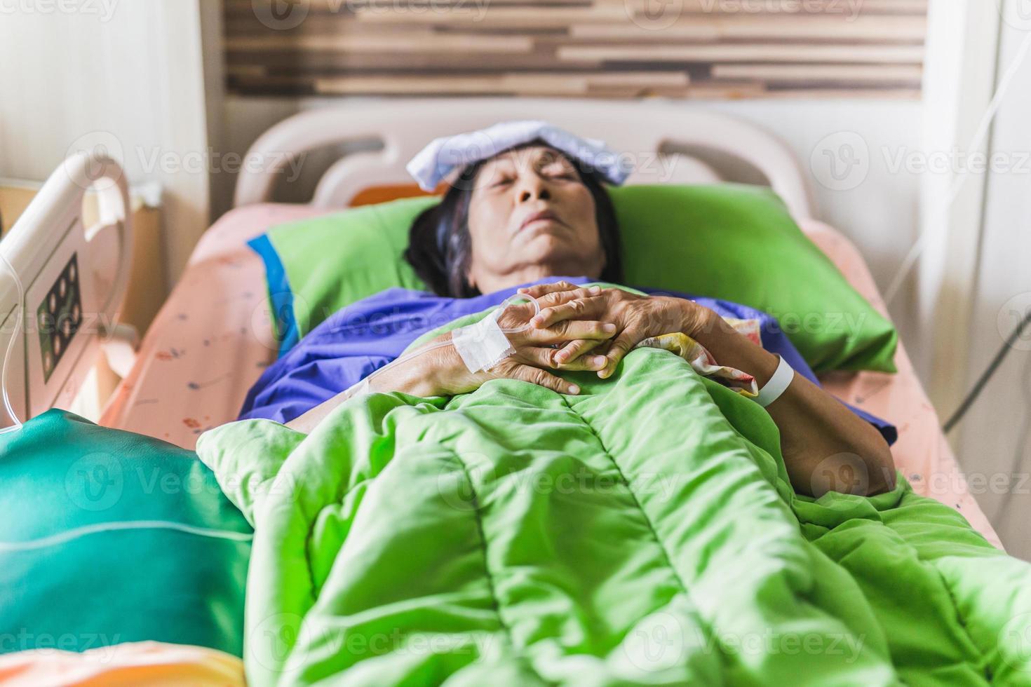 Mano del paciente senior con inyección de solución salina acostado en la cama de un hospital foto