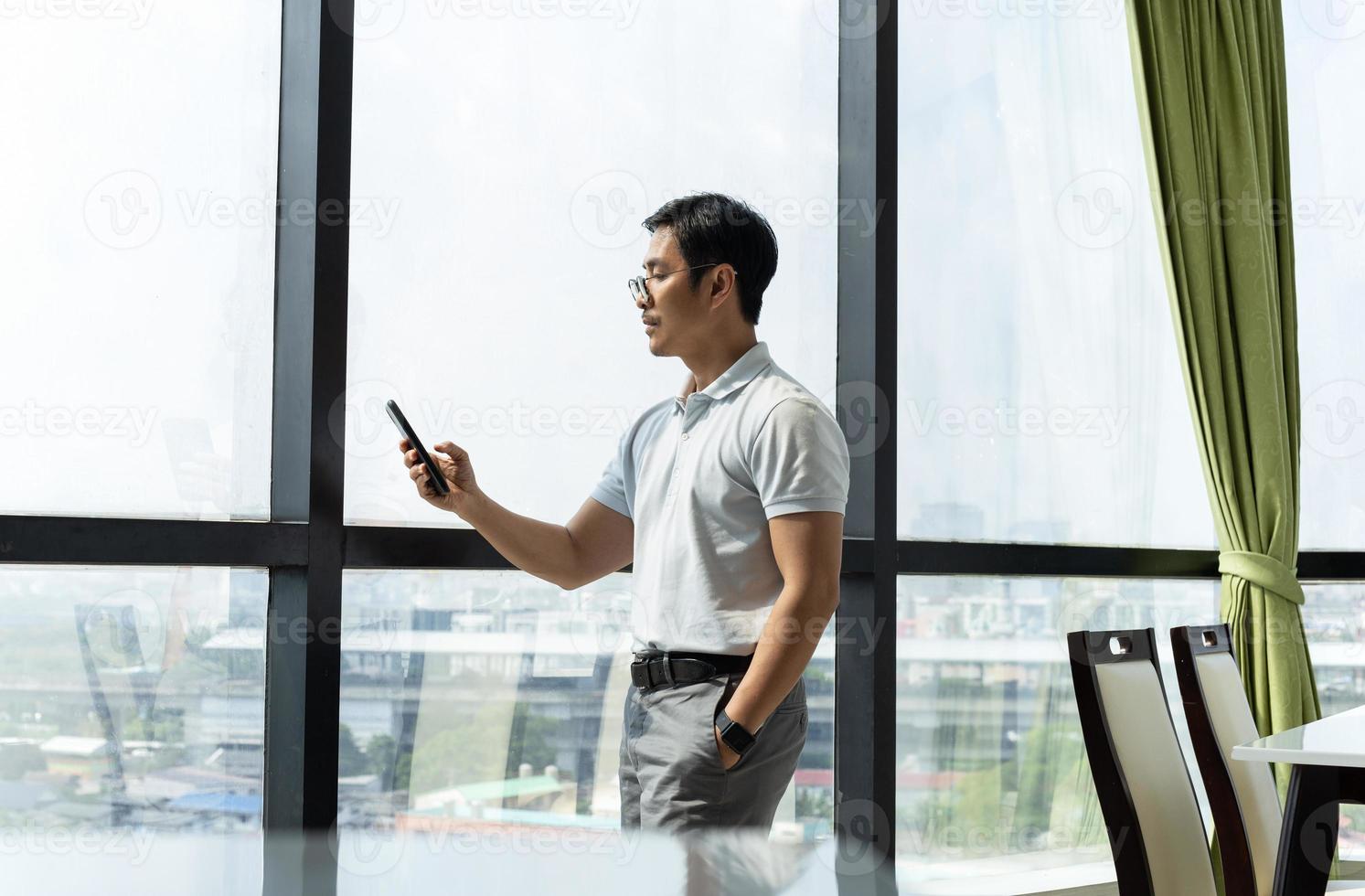 Businessman standing in office building window looking at cell phone photo