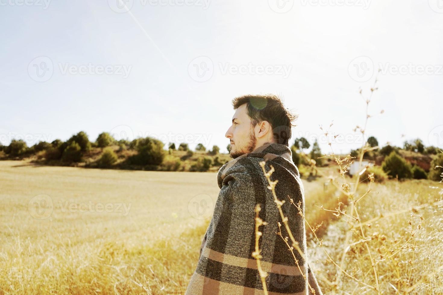 Lado de un stand joven disfrutando en calma el sol de otoño de la mañana en un camino de un campo amarillo con la luz de fondo del cielo azul foto