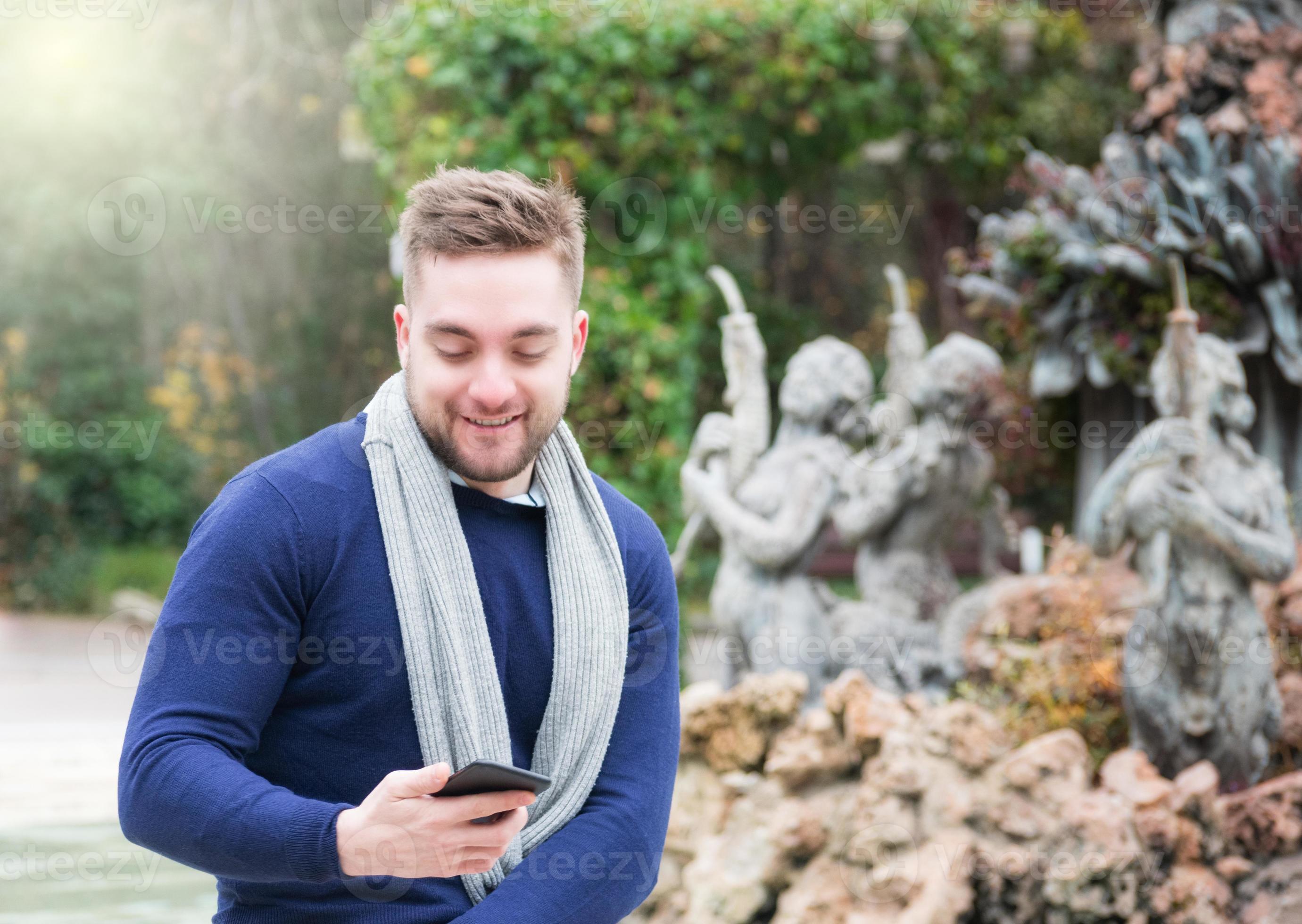 Young man smiling in a park checking his cell phone photo