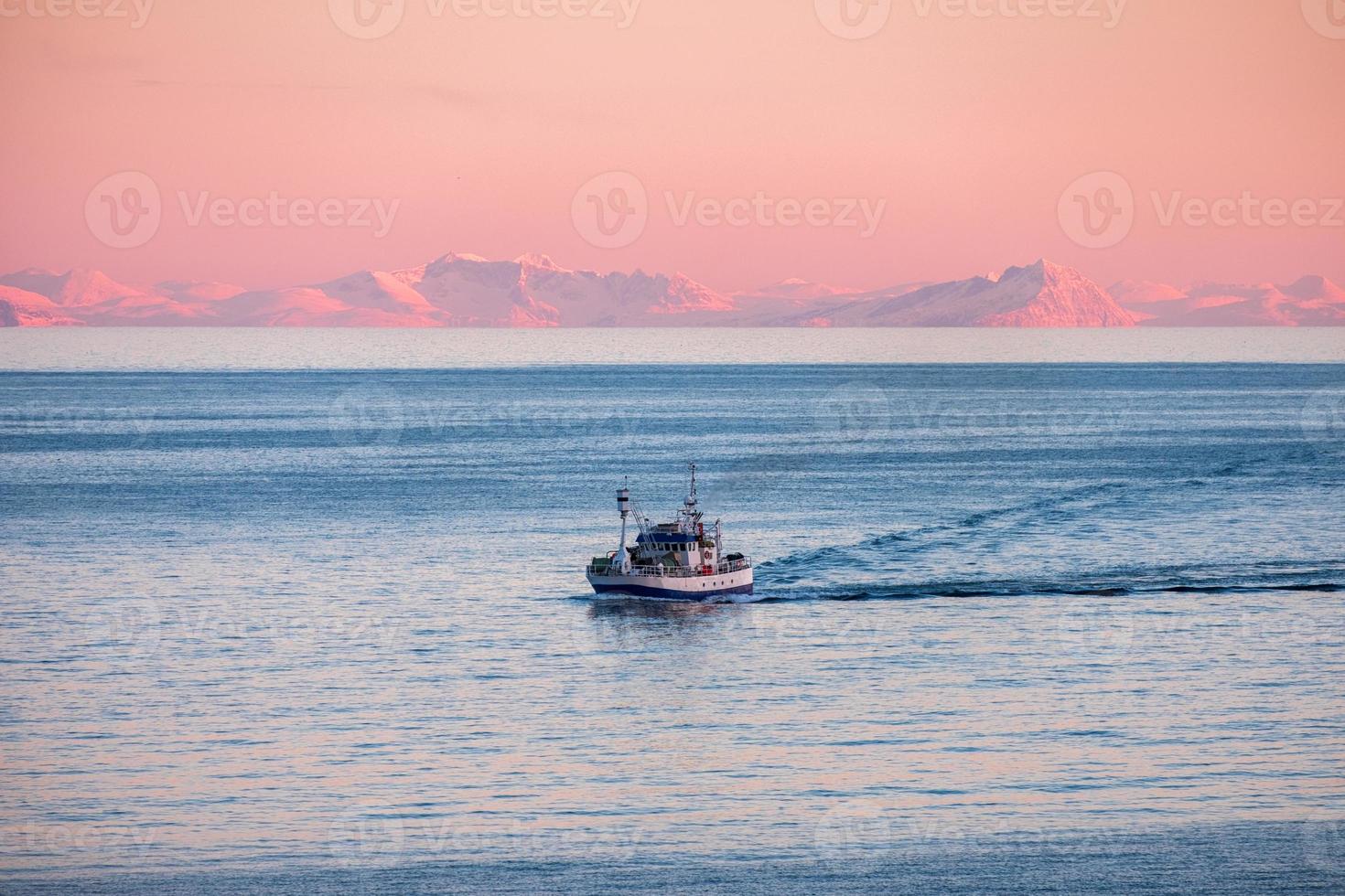 Fishing boat cruising on arctic sea to fish at sunset in winter photo