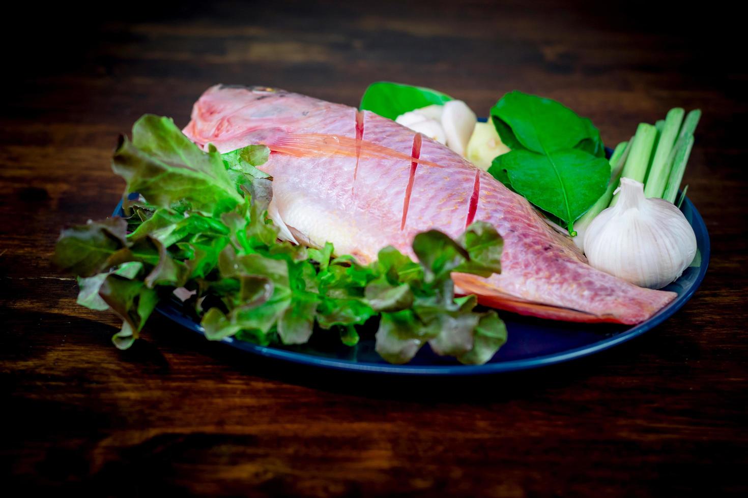 Primer plano de un pescado fresco y verduras en platos de cerámica preparados para cocinar foto