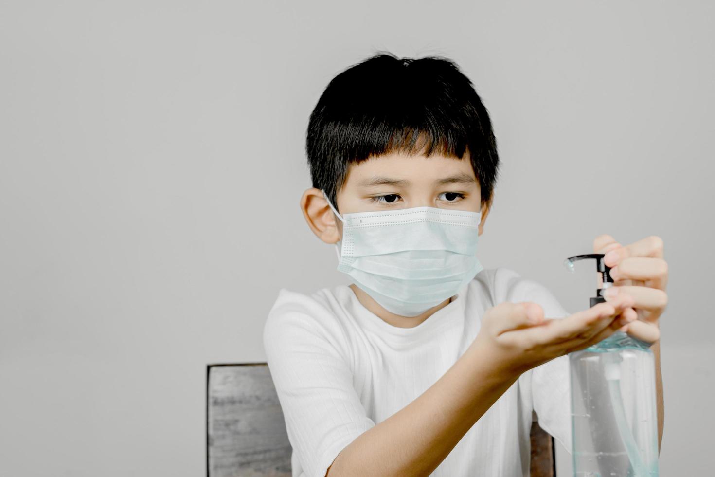 Primer plano de una cara de niño vistiendo una mascarilla de compresa sanitaria y lavándose las manos con gel de alcohol foto