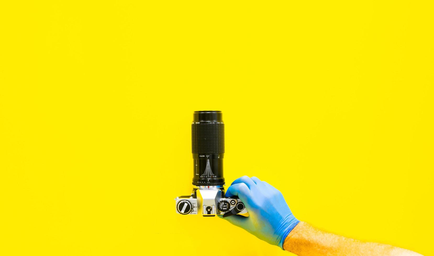 Hand with blue gloves holds vintage camera on yellow background photo