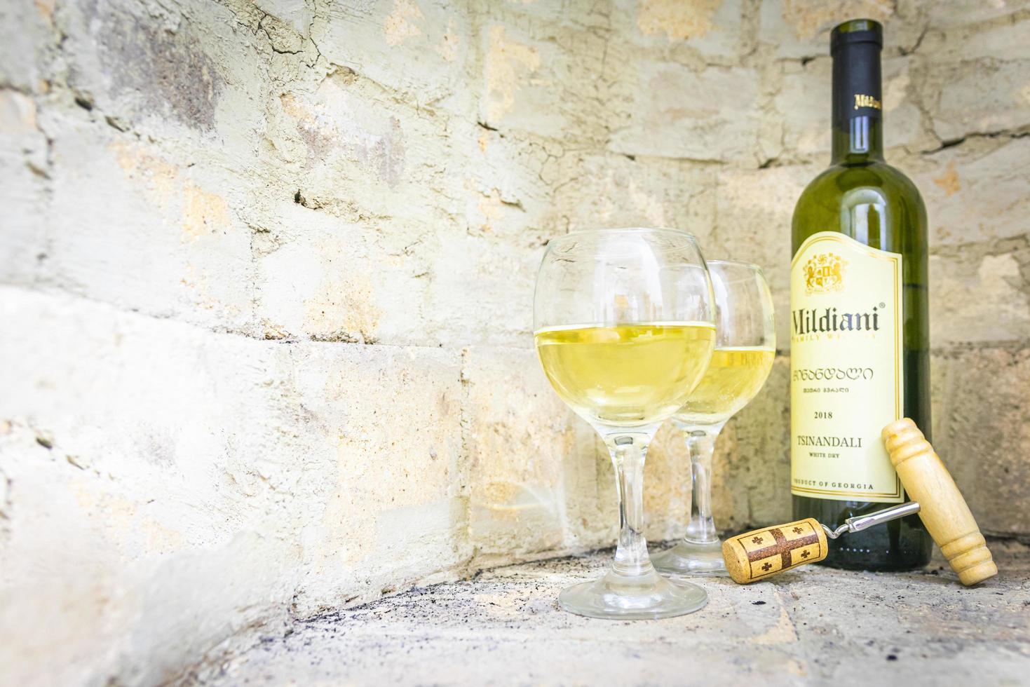 Setup of Georgian white wine Mildiani with cork and two full glasses in bright brick wall background photo