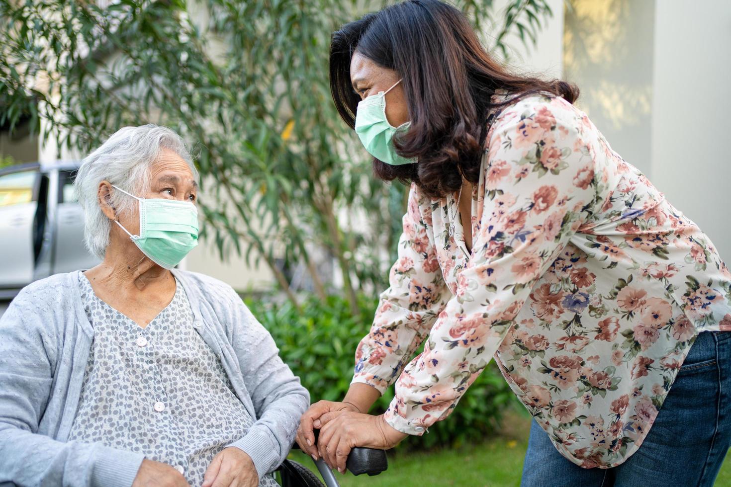 Ayude a la anciana asiática mayor o anciana en silla de ruedas y con una mascarilla para proteger la infección de seguridad covid 19 coronavirus en el parque foto