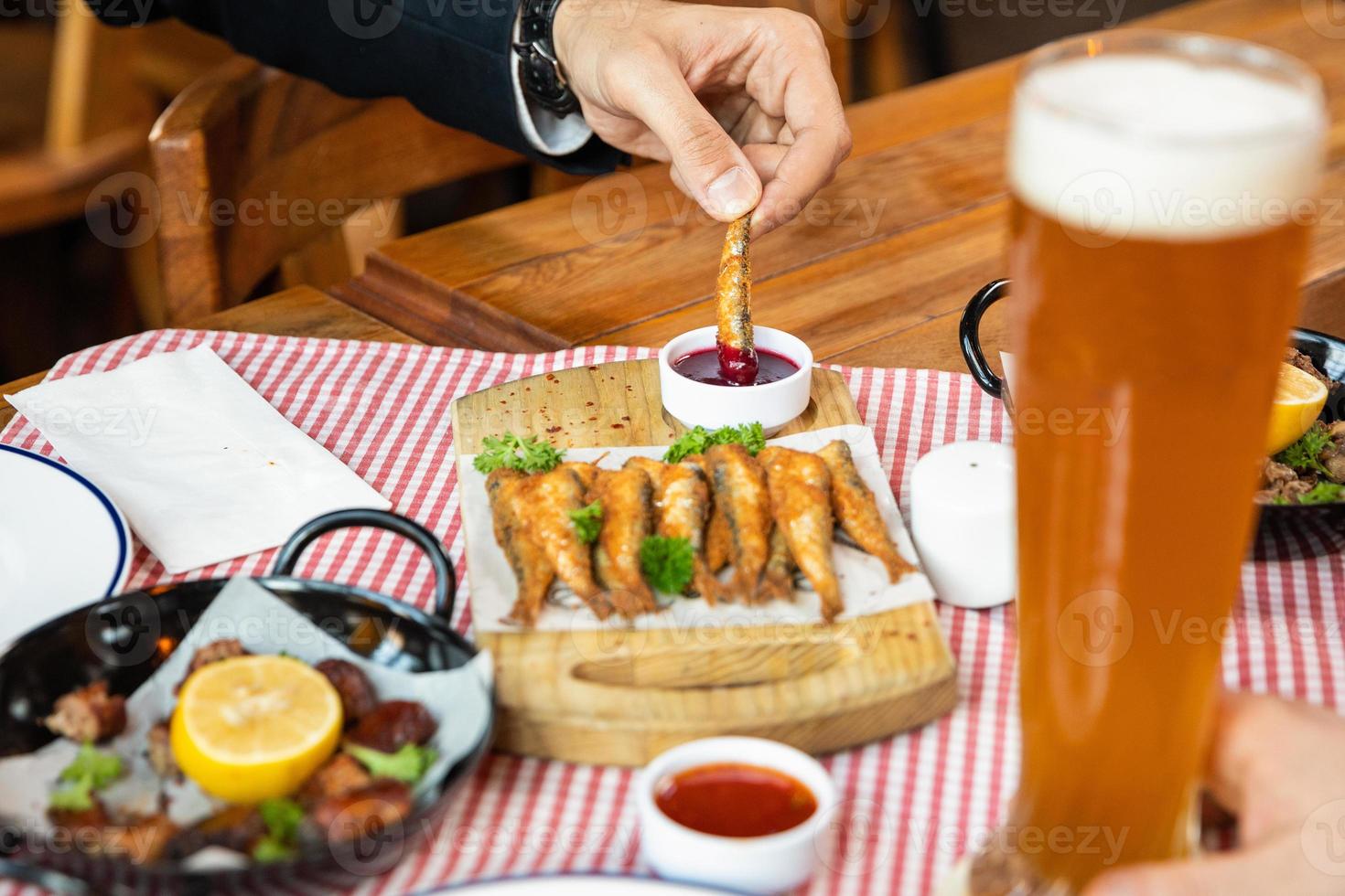 Man dipping Kilka, Sprat fish into ketchup close up photo