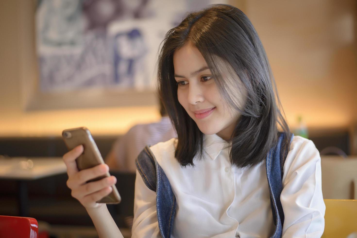 Mujer atractiva comprobar sus mensajes en el teléfono inteligente mientras está sentado en la cafetería. foto