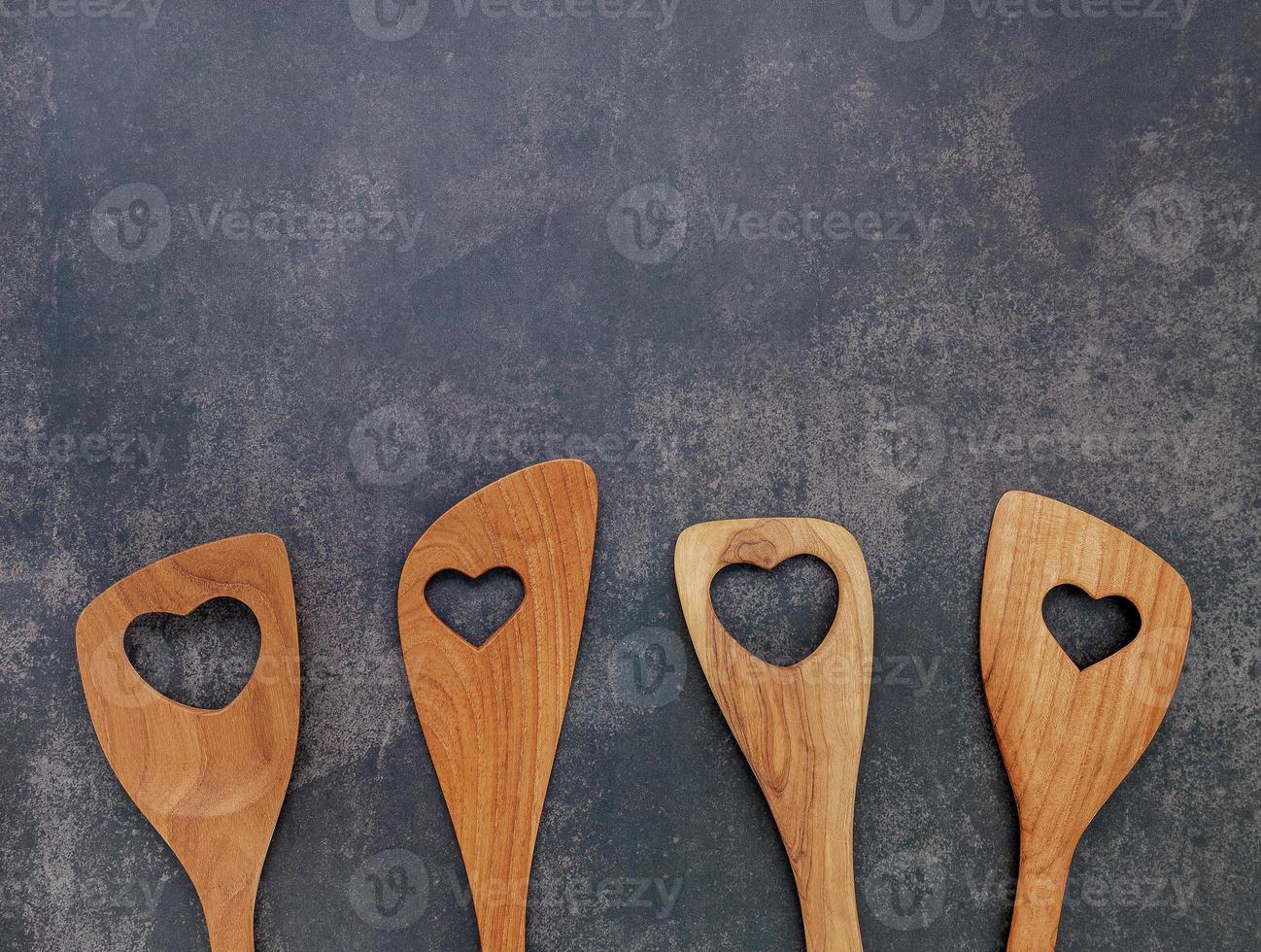 Varias en forma de corazón de utensilios de cocina de madera cucharas de madera y espátula de madera sobre fondo de hormigón con espacio plano y copia foto