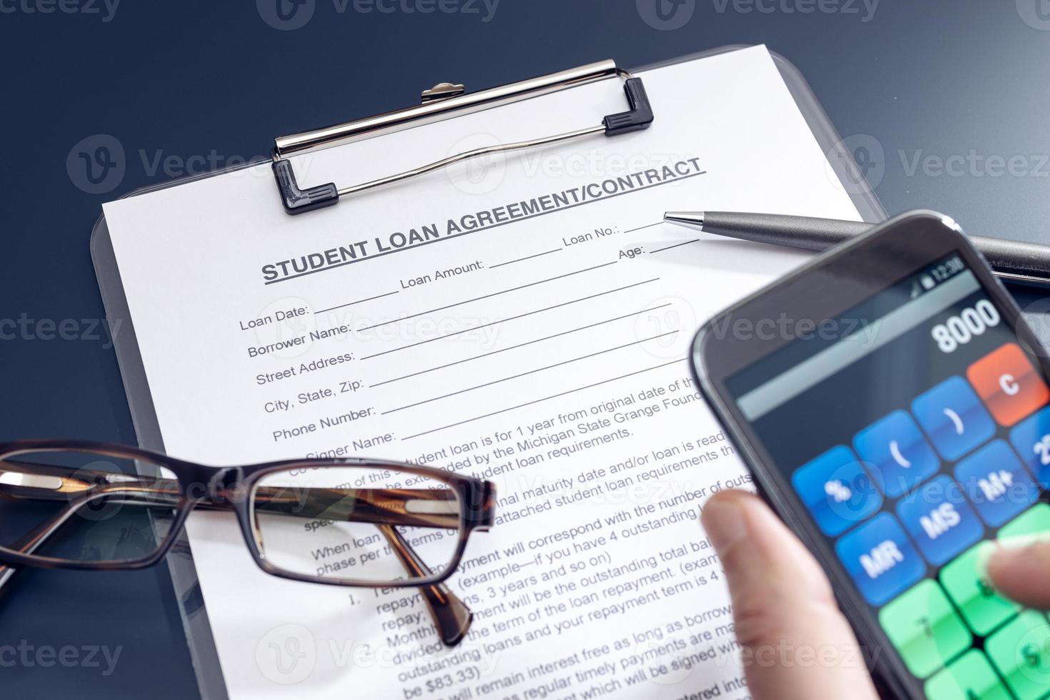 Blank Student Loan Application on table and hand holding a smartphone with calculator app photo