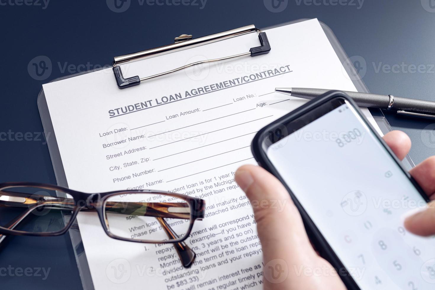 Blank Student Loan Application on table and hand holding a smartphone with calculator app photo