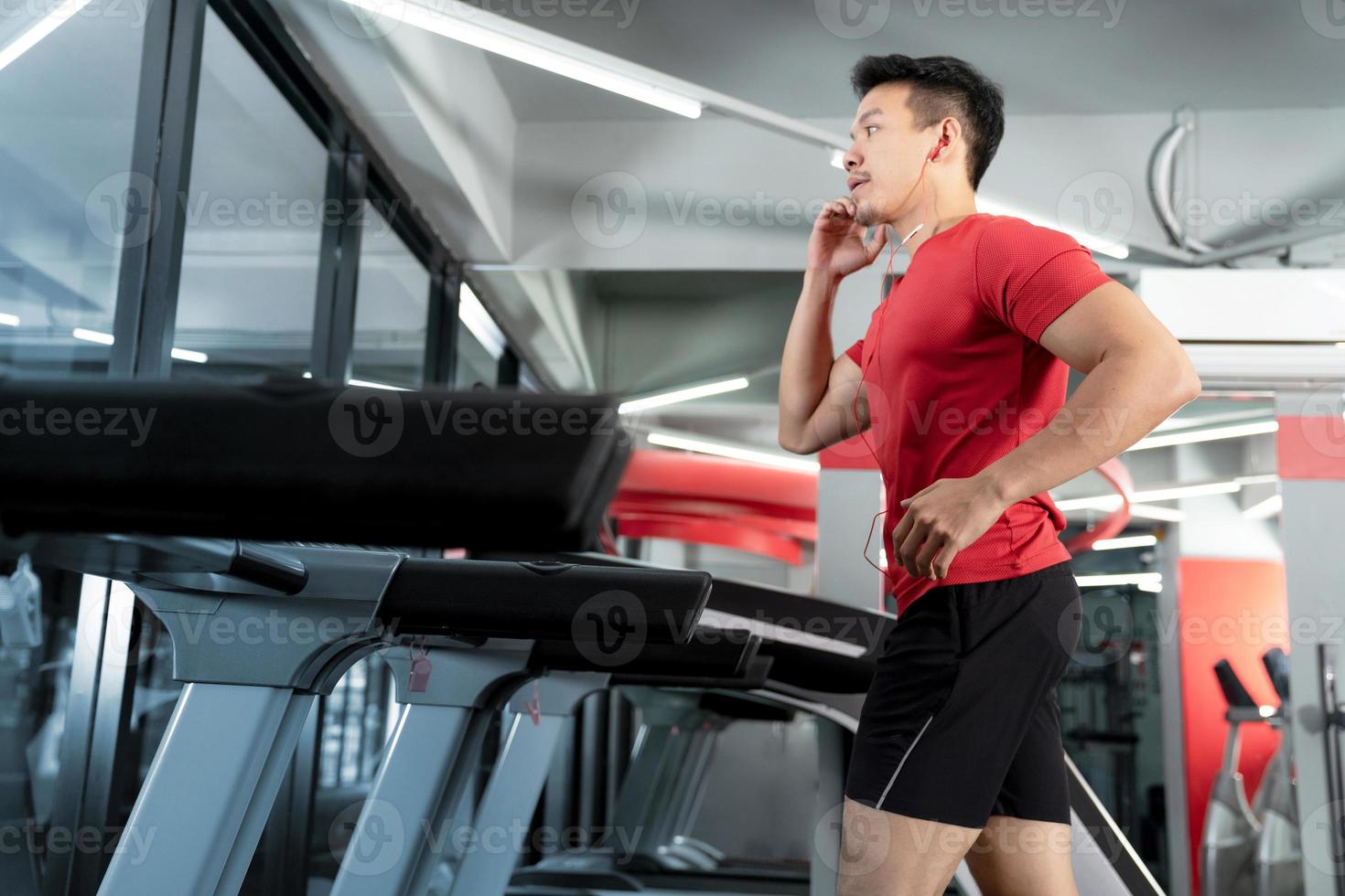 Athletic young man running and listening to music from his smartphone in gym photo