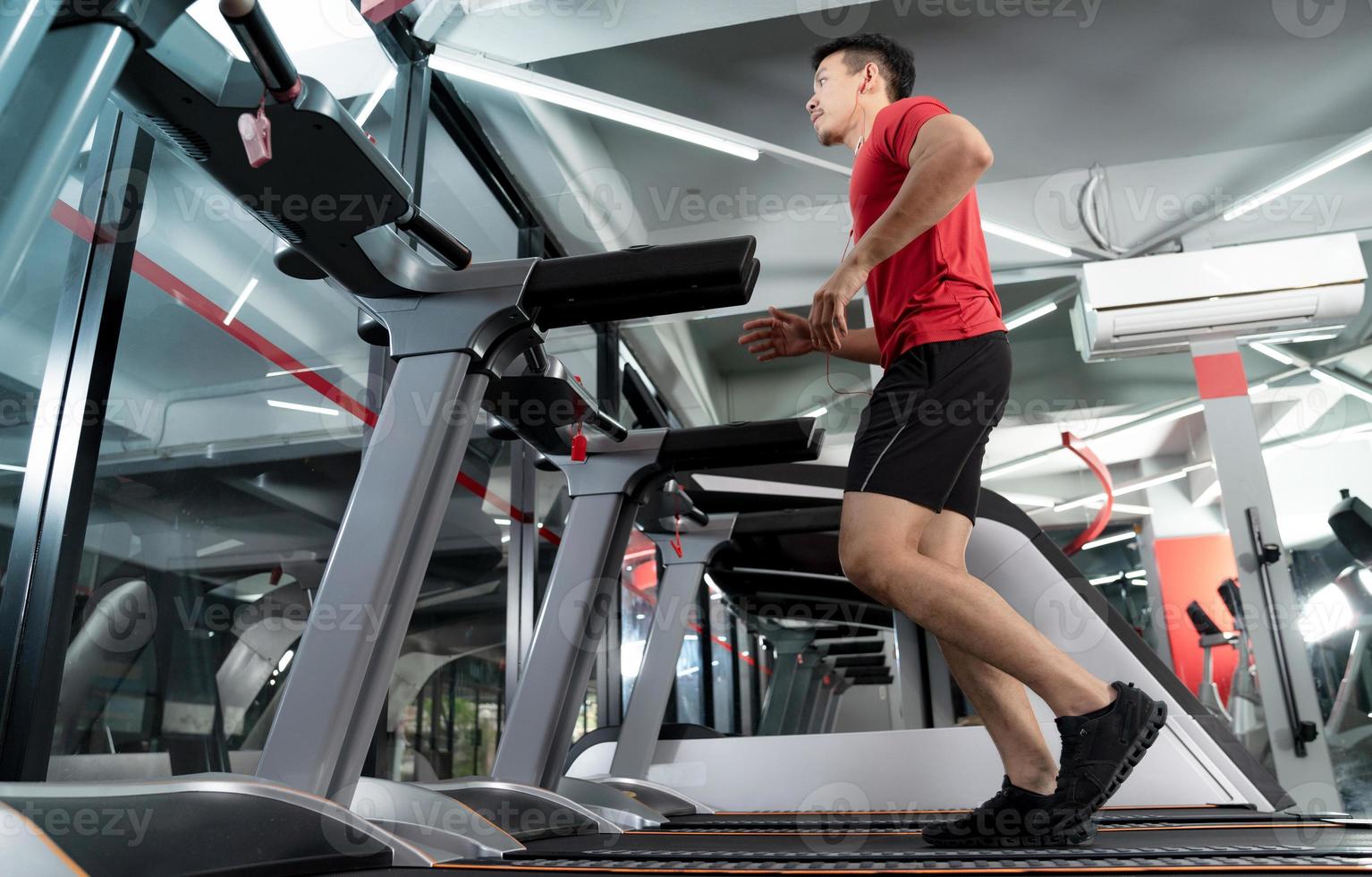 Athletic young man running and listening to music from his smartphone in gym photo