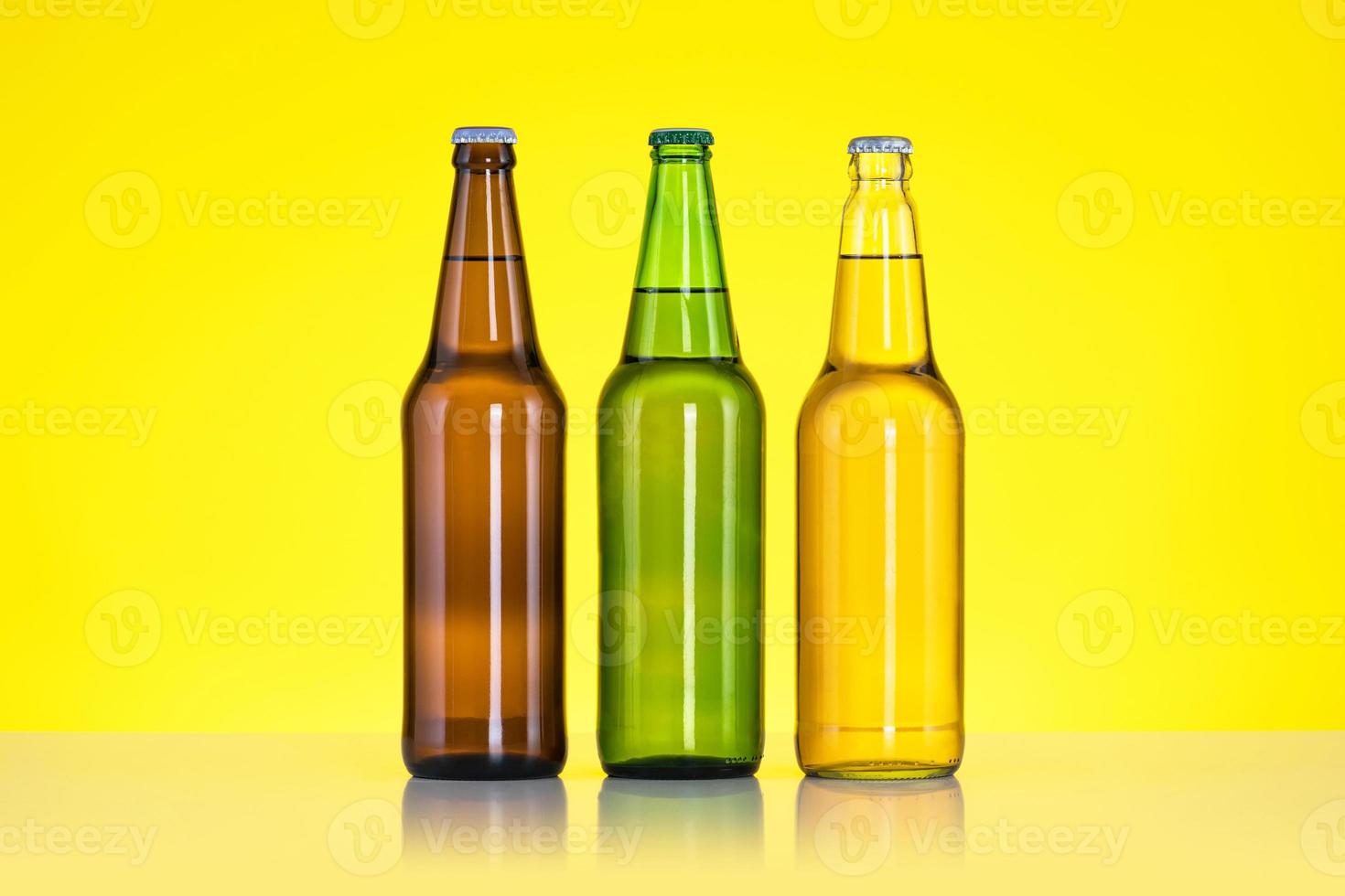 Grupo de tres botellas de cerveza aislado sobre fondo amarillo foto