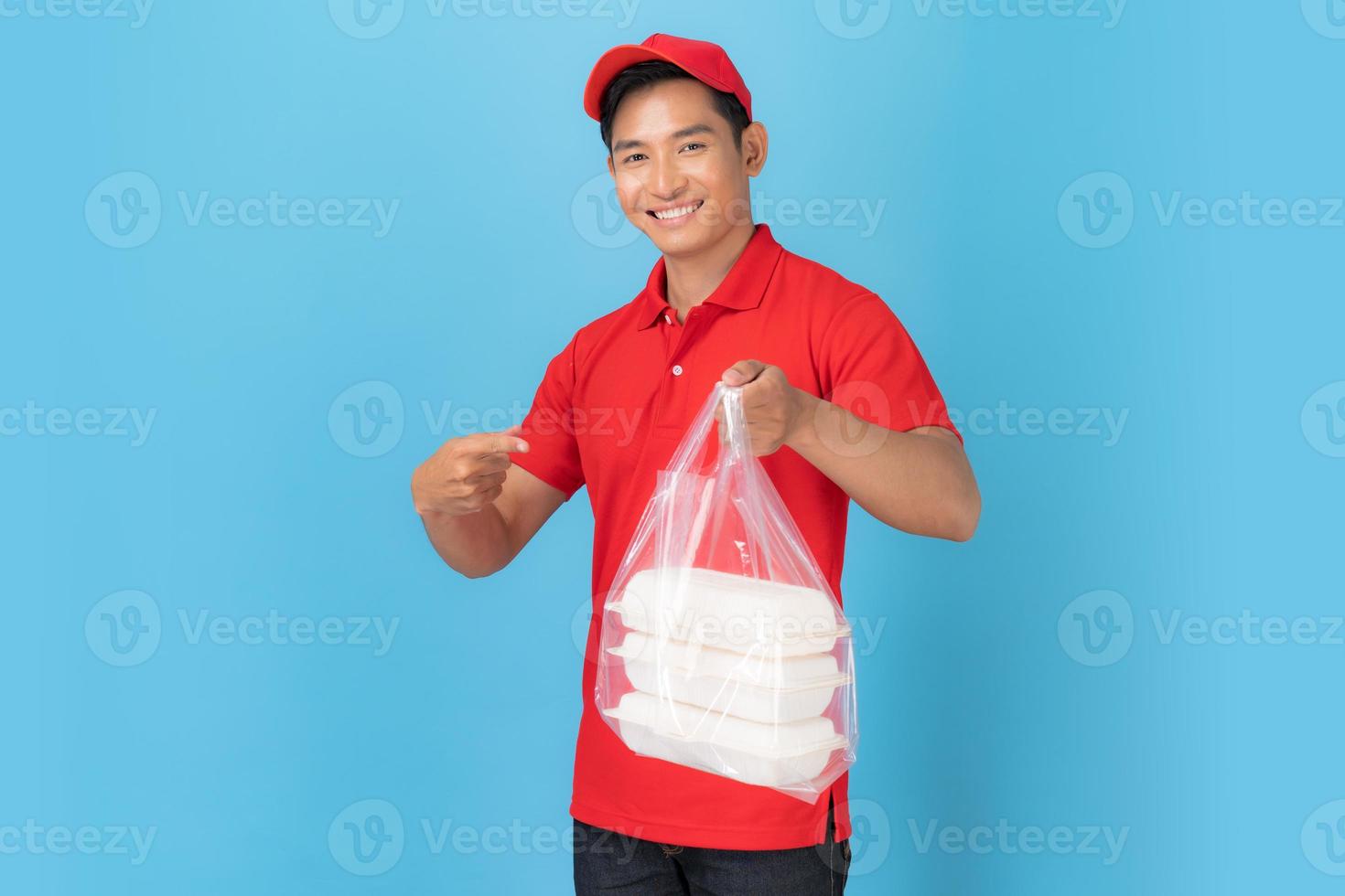 Repartidor sonriente empleado en gorra roja camisa en blanco uniforme de pie con dar orden de comida foto