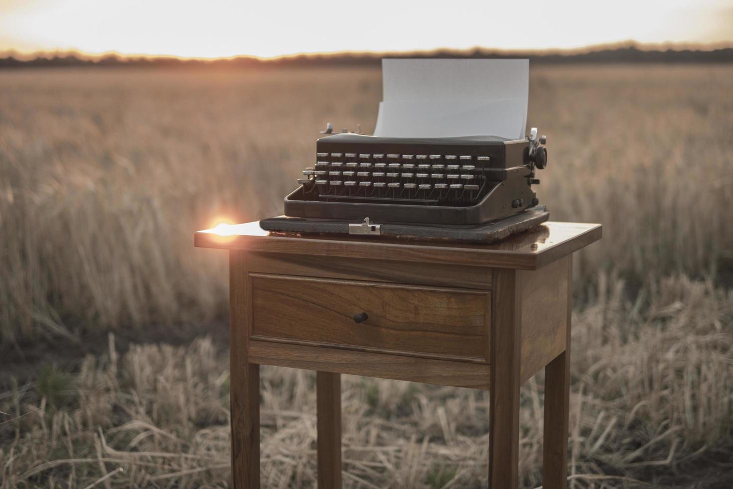 typewriter on a walnut bedside table in a wheat field at sunset photo