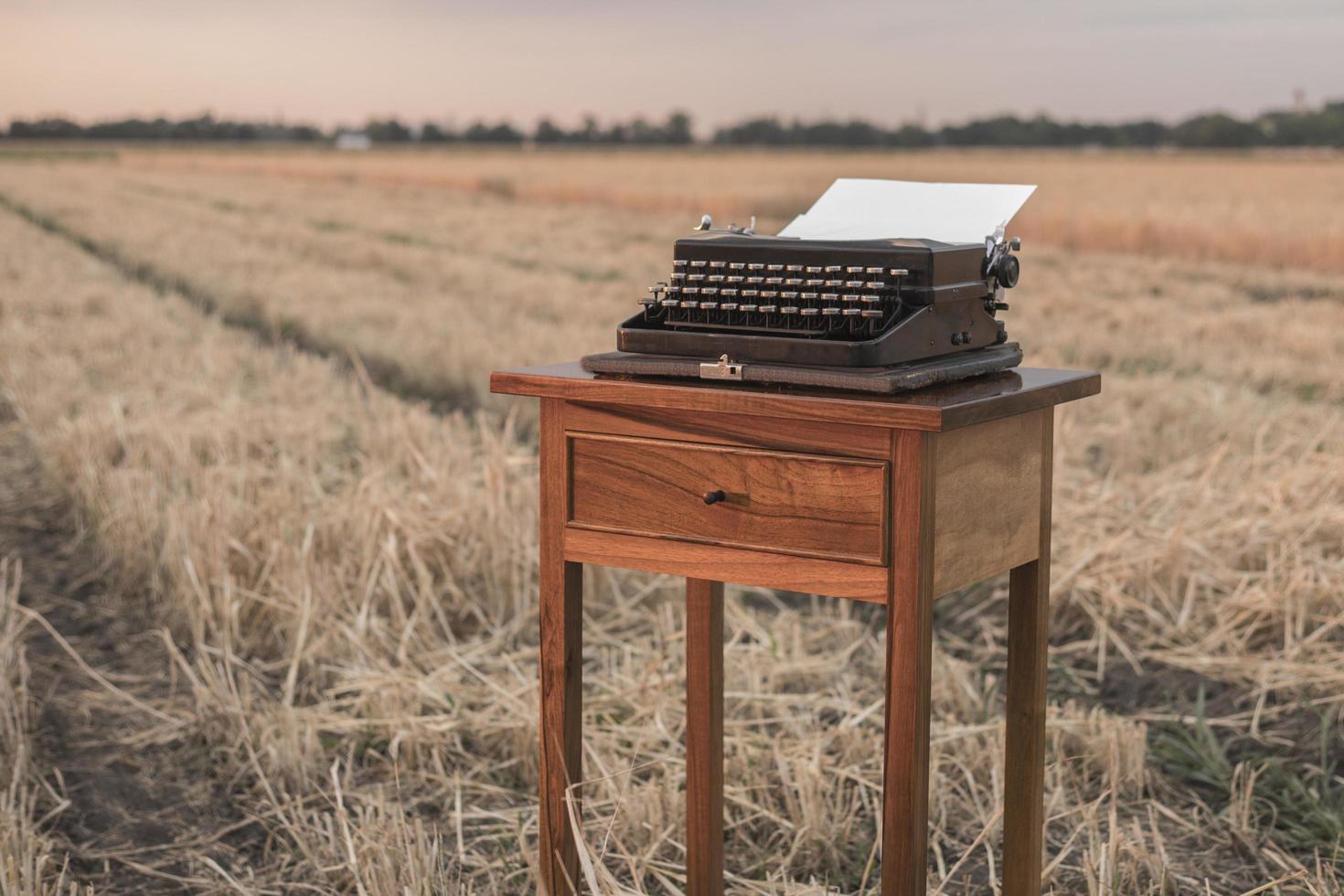 typewriter on a walnut bedside table in a wheat field at sunset photo