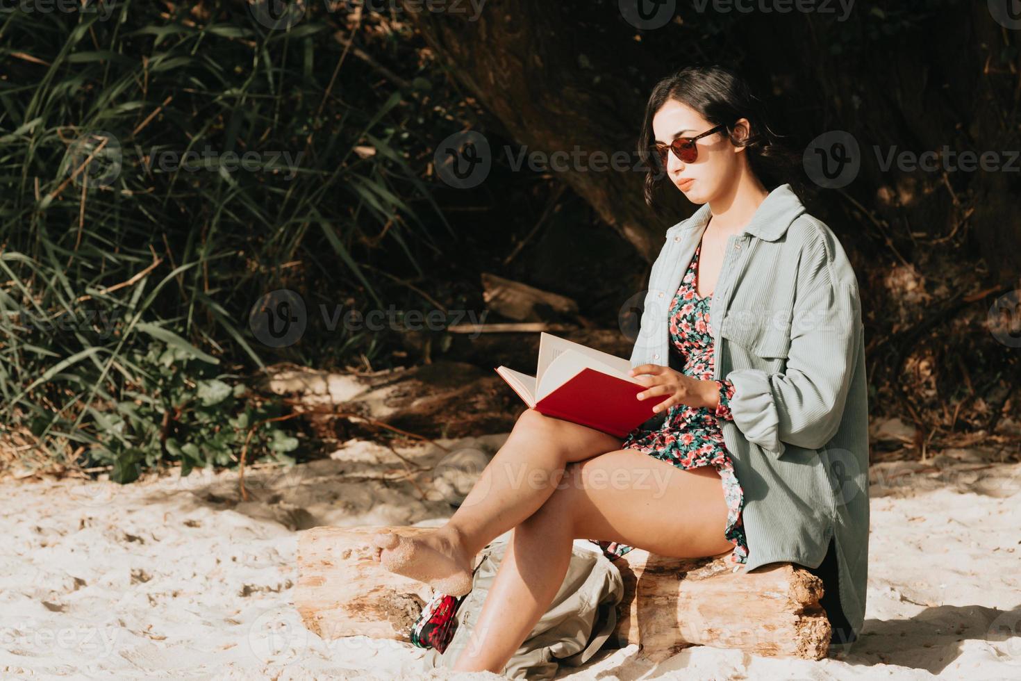 Joven mujer marroquí en ropa moderna sentada en la playa leyendo un libro Foto de stock en Vecteezy