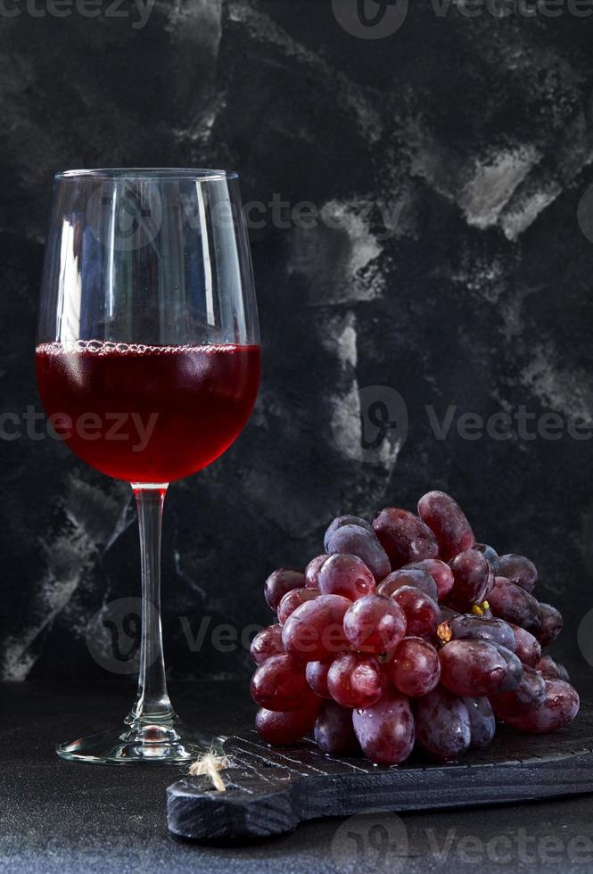 Copa de vino con uvas en un soporte de madera negra foto