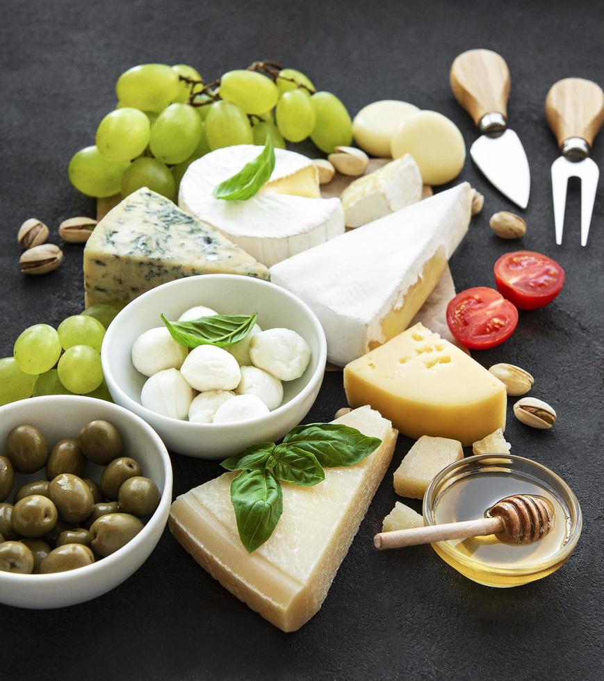 Various types of cheese, grapes, honey, and snacks on a black concrete background photo